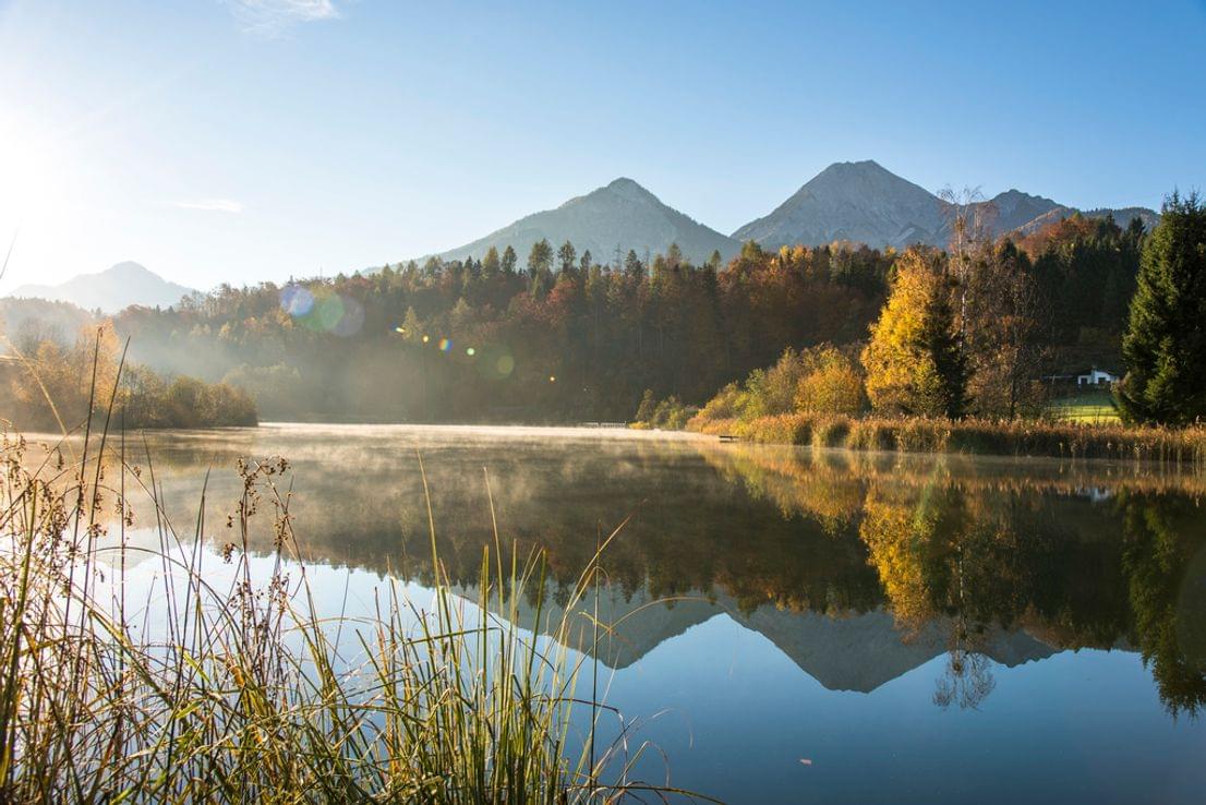 Bergsee mit Herbstwaldspiegelung unter klarem blauen Himmel